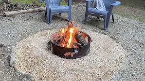 Two Adirondack chairs around a metal fire pit with a gravel ring, set in a forested area with string lights. - Private + Wooded + Quaint & Cozy + 5 mins to Dwntn Blk Mtn + 15 mins to Ashvle (Black Mountain)