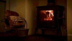 Ein traditioneller Holzofen mit Feuer, ein Metallstuhl und ein Holztisch in einem gemütlich beleuchteten Raum.