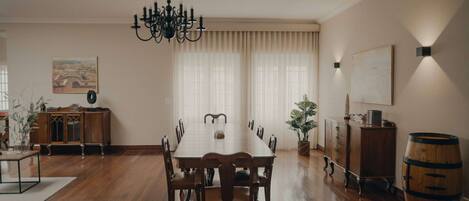 A dining room with a long wooden table, chairs, a chandelier, a cabinet, and a potted plant.
