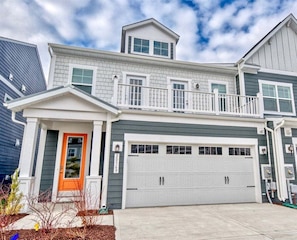 A two-story house with a garage, a balcony, and a distinct orange front door.