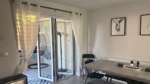 Een moderne woonruimte met een schuifdeur naar een buitenruimte, een eettafel met stoelen en een klein bijzettafeltje met decoratieve items.