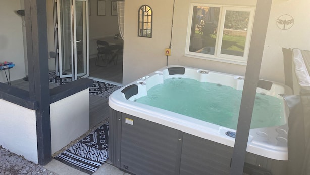 Een hottub met glazen omheining, een terrasgedeelte met een versierde vloerkleed en uitzicht op de achtertuin door een schuifdeur.