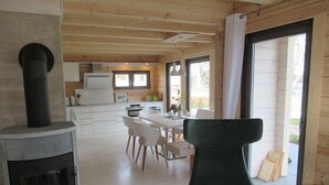 A modern kitchen with white cabinets, a black stove, and a dining area with white chairs and a green sofa. - Haus Seeblick, directly on the shore of the Gr. Lake Zechlin (Rheinsberg)