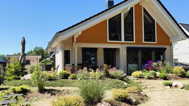 A modern house with a prominent gable roof, large windows, and a well-maintained garden with various plants and flowers. - Haus Seeblick, directly on the shore of the Gr. Lake Zechlin (Rheinsberg)