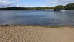 A sandy beach with calm water, a small boat, and a forested area in the background. - Haus Seeblick, directly on the shore of the Gr. Lake Zechlin (Rheinsberg)