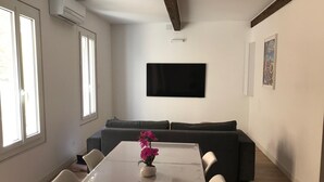 Ein modernes Wohnzimmer mit einem Esstisch, einem grauen Sofa und einem schwarzen Wand-Fernseher.