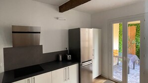 Eine moderne Küche mit weißen Schränken, einer schwarzen Arbeitsplatte und Edelstahlgeräten. Das Zimmer verfügt über eine Holzbalkendecke und eine Glastür, die zu einem Außenbereich führt.