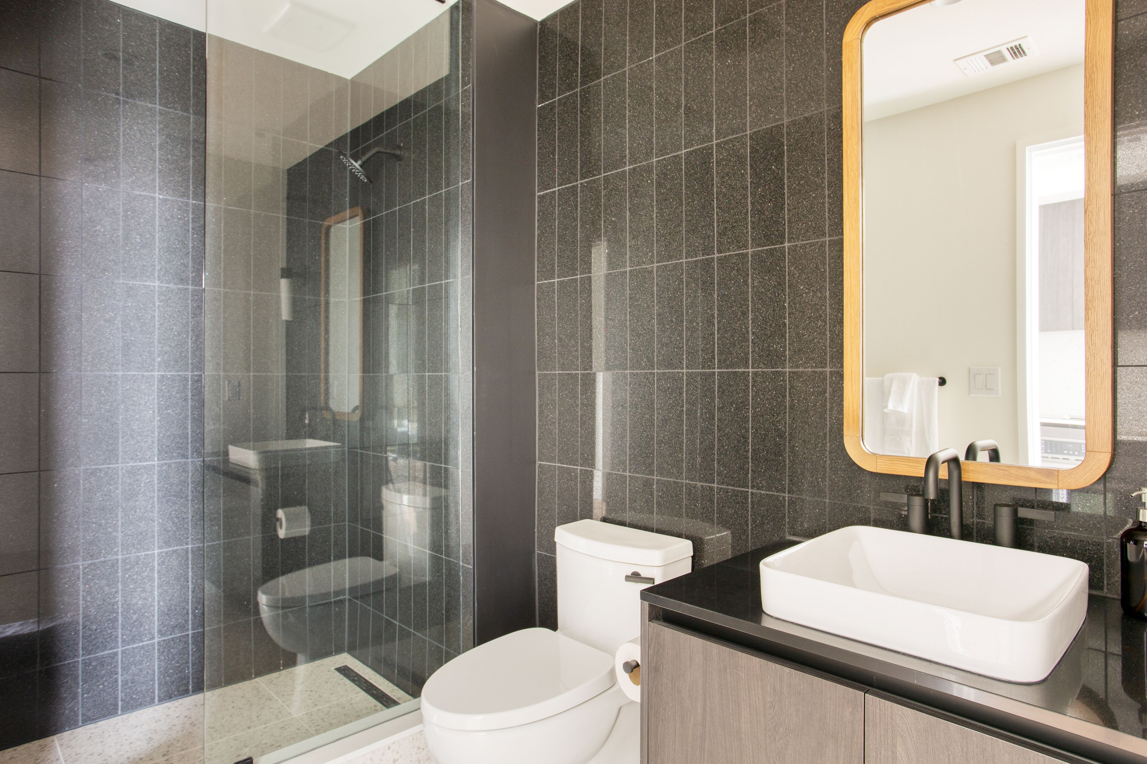 A modern bathroom with a glass-enclosed shower, a white toilet, and a rectangular sink with a mirror above it.