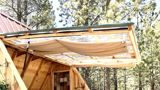 Una cabaña de madera con un dormitorio en el altillo, una cama, un ventilador y una terraza.