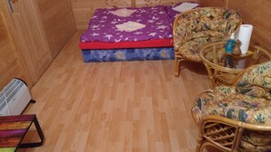 Ein kleines Zimmer mit Holzboden, einem Bett mit lila Sternenmusterdecke, zwei Korbstühlen und einem Tisch mit Toilettenartikeln.