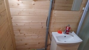 Ein kleines Badezimmer mit Holzwänden, einem weißen Waschbecken und einem grünen Toilettendeckel.
