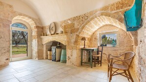 A rustic stone room with a table, chair, and a view through an arched doorway.