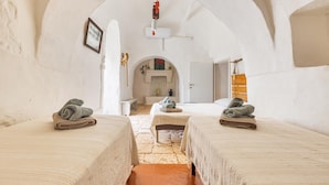 A room with two beds, a bench, and a fireplace. - Trullo Palma by Perle di Puglia (San Michele Salentino)