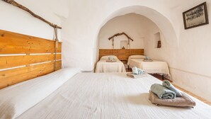 A room with a wooden headboard, two beds with white linens, a wooden archway, and a rustic wall decor. - Trullo Palma by Perle di Puglia (San Michele Salentino)