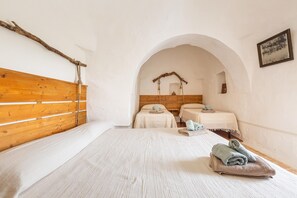 A room with a wooden headboard, two beds with white linens, a wooden archway, and a rustic wall decor. - Trullo Palma by Perle di Puglia (San Michele Salentino)