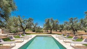 A rectangular pool with a clear blue water surface, surrounded by stone tiles and shaded by trees. - Trullo Palma by Perle di Puglia (San Michele Salentino)