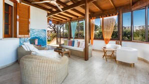 Una habitación iluminada por el sol, con muebles de mimbre, un ventilador de techo y ventanas grandes con cortinas.