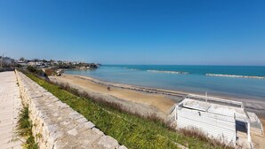 Vista costera con muro de piedra, playa y un pequeño edificio con techo de metal.