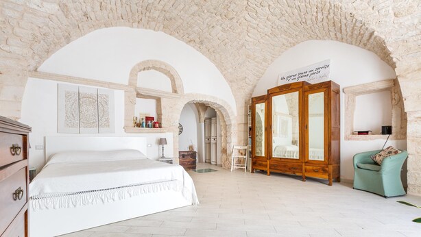 A bedroom with a large bed, a wardrobe, and a chair. There are arched ceilings and a stone wall. - Casa Chianchizze by BarbarHouse (Ceglie Messapica)