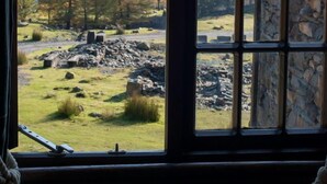 Ein Fenster mit Blick auf ein Steingebäude und eine Landschaft mit Bäumen und Hügeln.