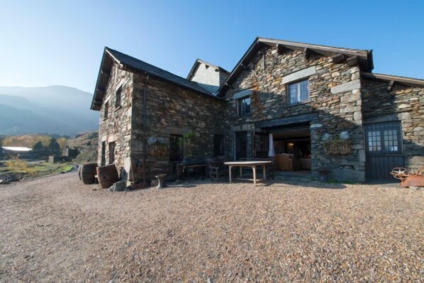 A stone building with a gravel driveway, outdoor seating, and a mountain view.