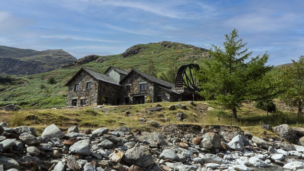 Ein Steinhaus mit Windmühle, umgeben von felsigem Gelände und Hügeln.