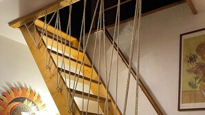 Una scala a chiocciola in legno con una scaletta e una sedia rossa con cuscino bianco, oltre a un decoro a forma di sole fissato al muro.