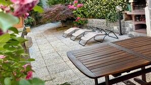 Zona patio con tavolo, sedie, barbecue e parete di piante fiorite.