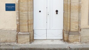 Una puerta doble blanca con una celosía metálica decorativa, ubicada dentro de un arco de piedra. Un cartel sobre la puerta dice 