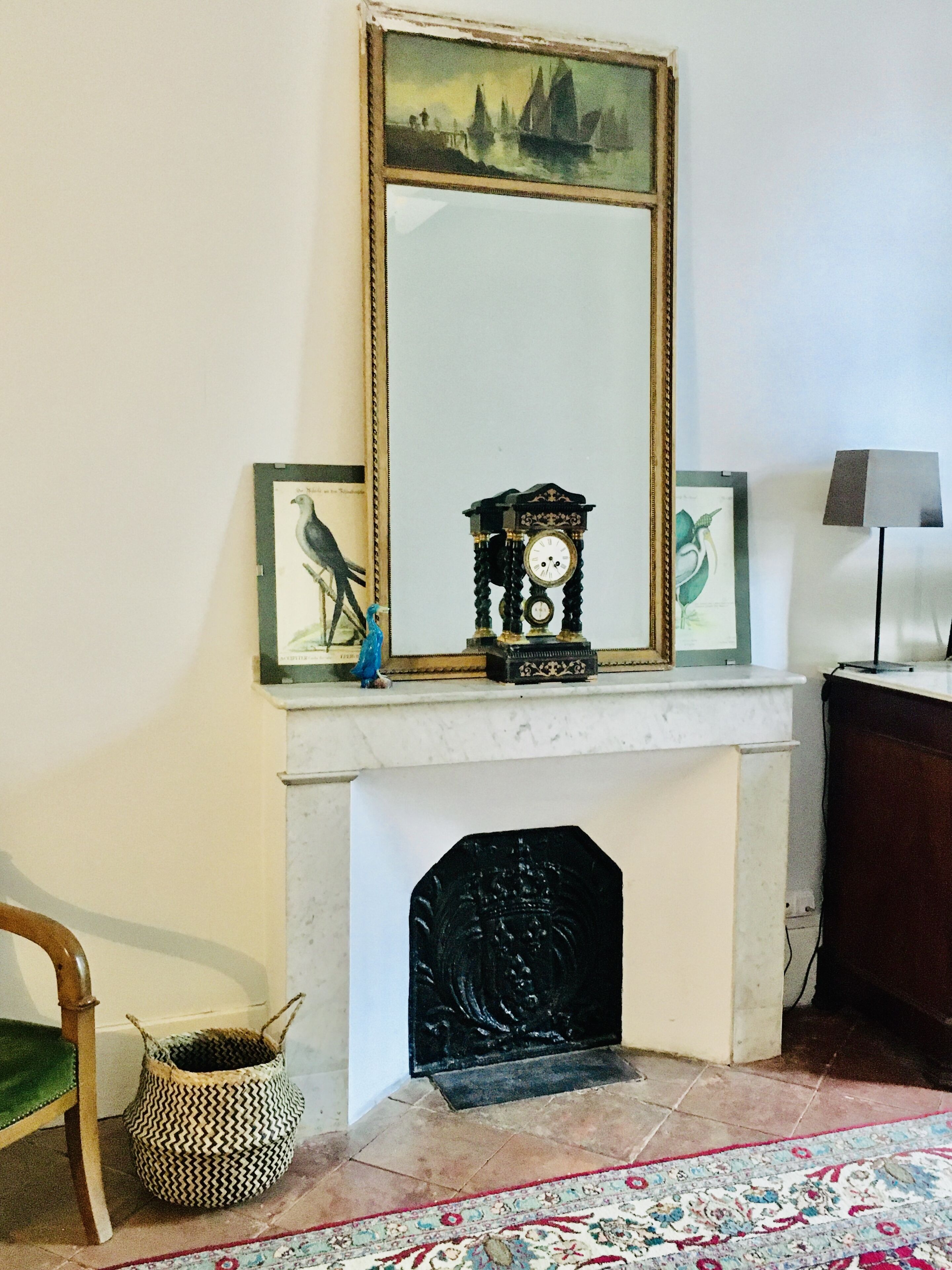 Una habitación con chimenea, espejo, reloj y lámpara.