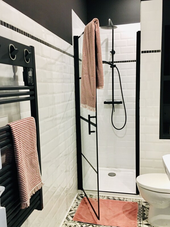 Un baño moderno con ducha envuelta en cristal, toallero negro y váter blanco.