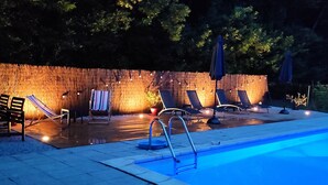 Una piscina con sillas de descanso y un muro de madera con luces colgantes.