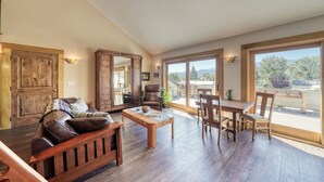 Un salón amplio con piso de madera, un sofá de cuero, una mesa de comedor con sillas y puertas correderas de vidrio que dan a una terraza exterior.
