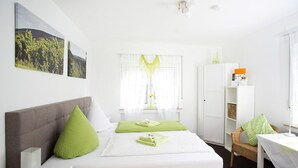 Un dormitorio ordenado con cama, mesita de noche, silla, armario y ventana con cortinas.