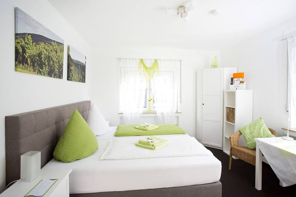 A neatly arranged bedroom with a bed, a bedside table, a chair, a wardrobe, and a window with curtains.