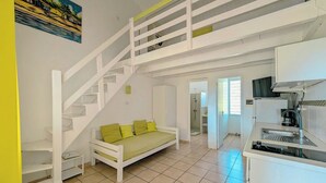 A spacious living area with a white staircase, a sofa with green cushions, and a kitchen area. - Bungalow (Saint-François)
