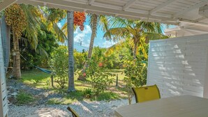 A covered outdoor area with a table and chairs, surrounded by palm trees and a white fence. - Bungalow (Saint-François)