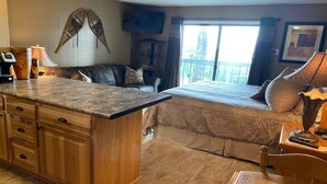 Une chambre d’hôtel compacte comprenant un coin cuisine, un lit, un espace salon avec un canapé et un balcon avec vue.