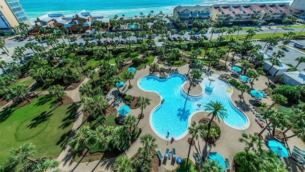 Un resort con una piscina grande, palmeras y vistas al océano.
