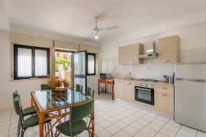 A modern kitchen with a dining area, a ceiling fan, and a view through the open door.