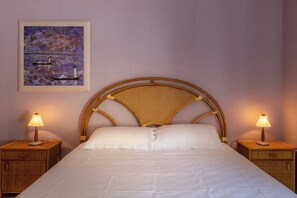 A bed with white linens, a wicker headboard, two bedside tables with lamps, and a framed artwork on the wall.