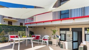 Eine überdachte Terrasse mit Tisch und Stühlen, ein Balkon mit Geländer sowie eine Tür mit Fenster.