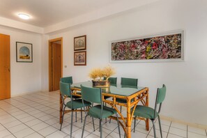 Un coin repas avec une table et des chaises, des œuvres d’art encadrées au mur et une porte visible au fond.