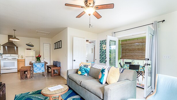 A living room with a sofa, a dining table, and a kitchen area in the background. - Jungle Bungalow - A lovely space to stay for island fun! (Keaau)