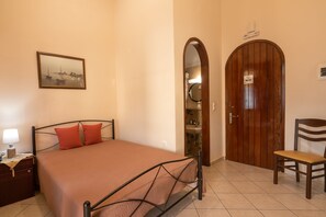A bedroom with a bed, a nightstand, a chair, a wooden door, and a mirror.