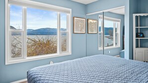 Ein Schlafzimmer mit einem großen Bett, zwei Fenstern, einem Deckenventilator und Blick auf Berge und Wasser.