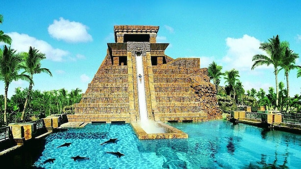 Una gran estructura piramidal con un tobogán que lleva a una piscina rodeada de palmeras.