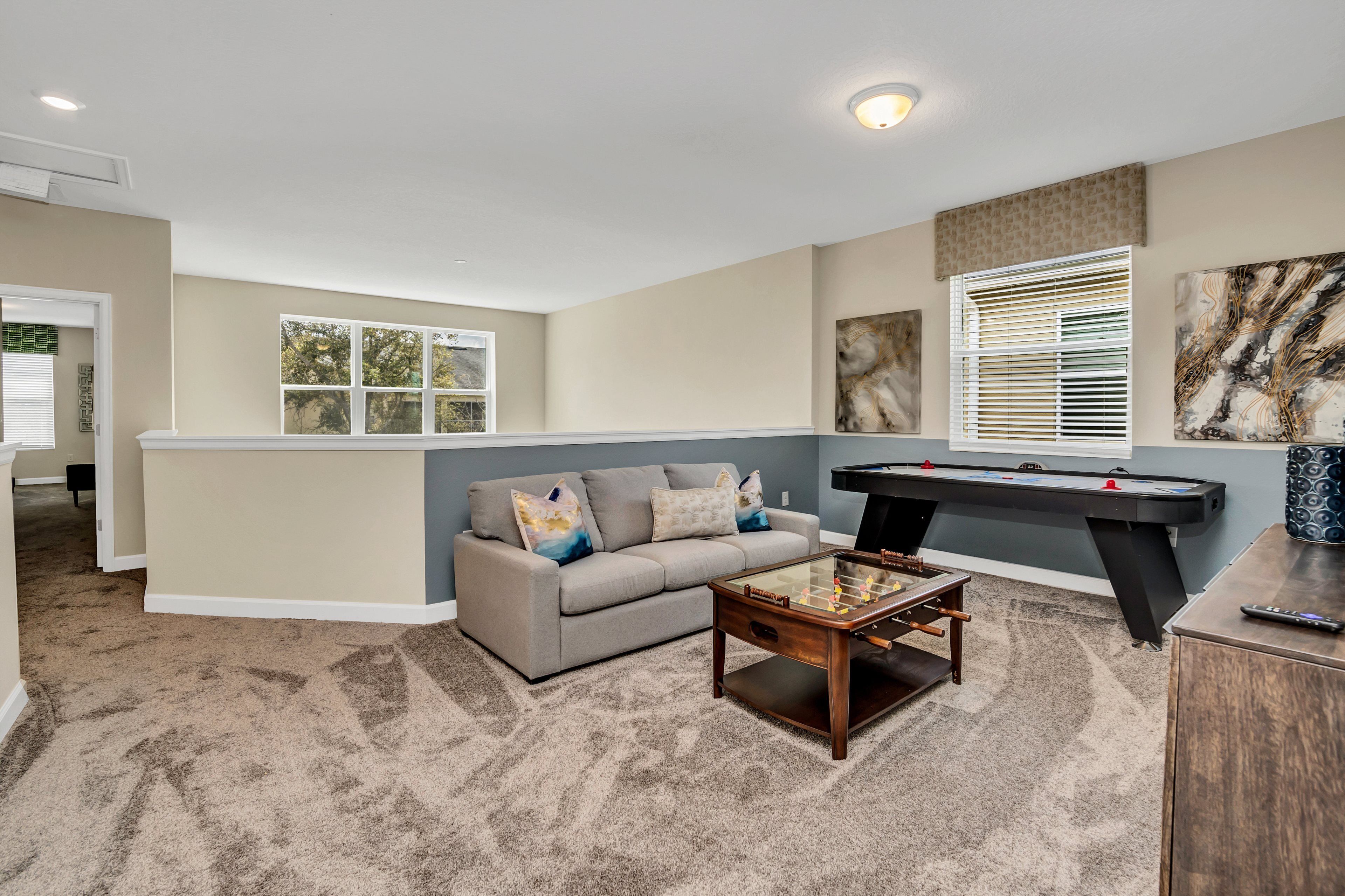A living room with a sofa, coffee table, foosball table, and a pool table.