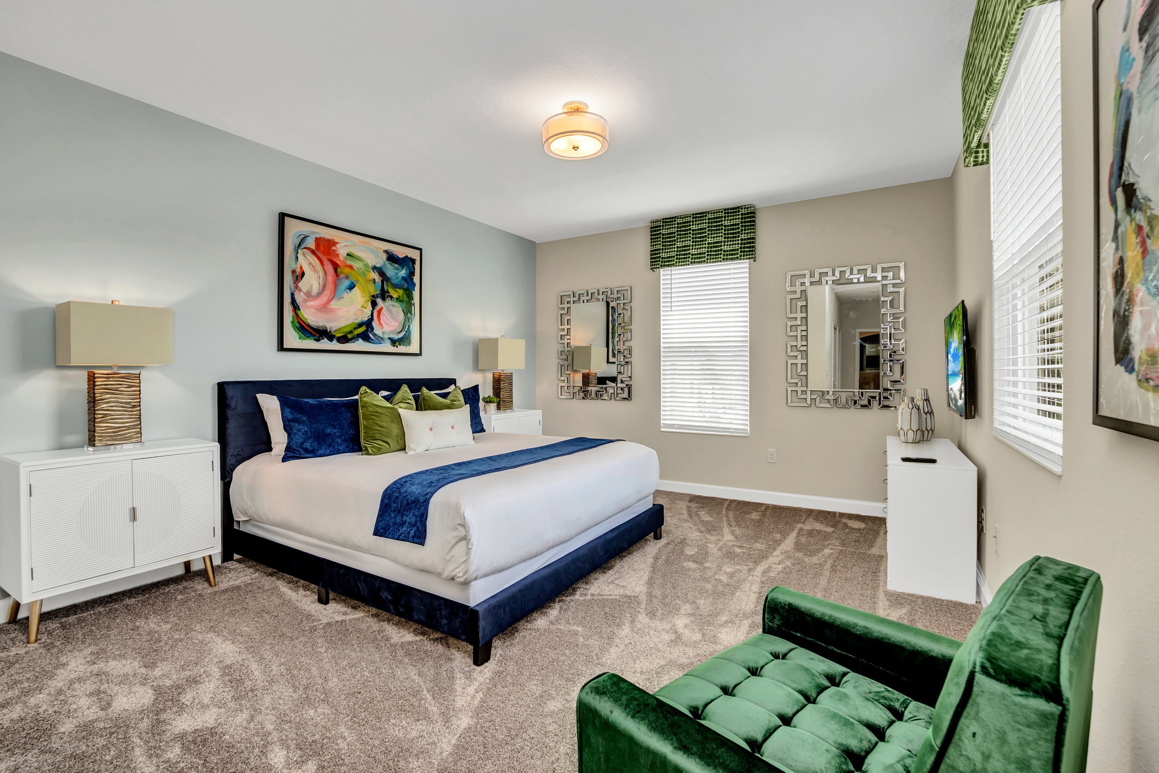 A bedroom with a large bed, a green chair, a white dresser, and a painting on the wall.