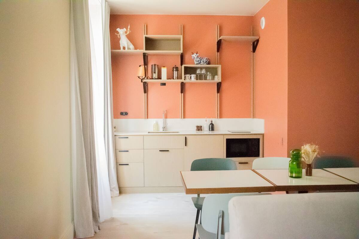 A compact kitchen with white cabinets, a countertop, and a dining area with two chairs.
